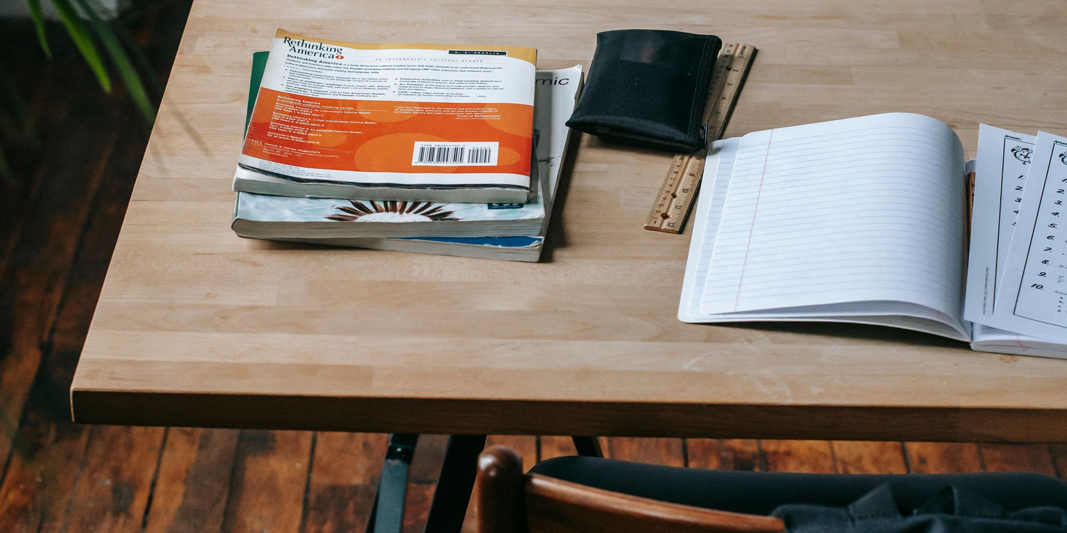 School desk with textbooks, a notebook, and a backpack on the chair