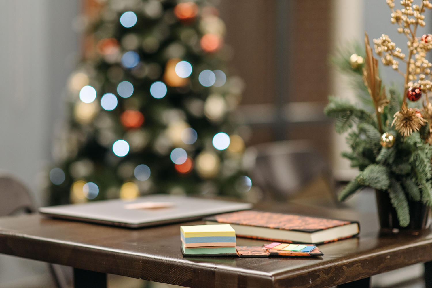 Desk with a laptop, notebook, and sticky notes, with a lit Christmas tree in the background