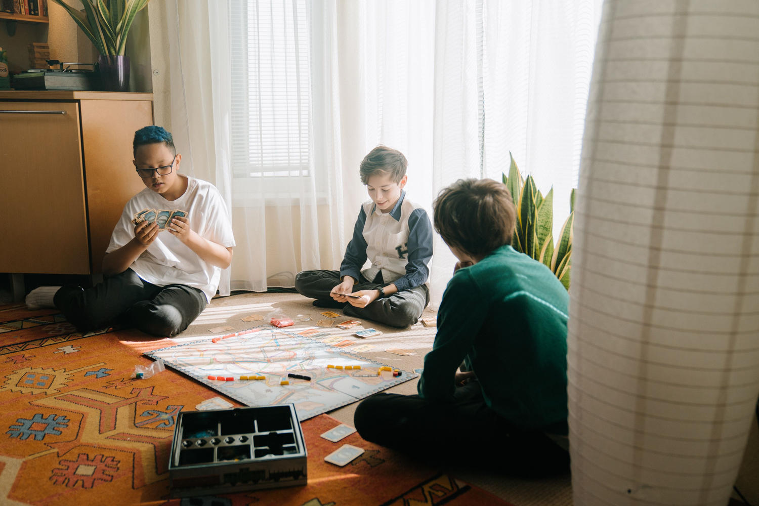 Three kids sitting on the floor playing a board game together by a sunlit window