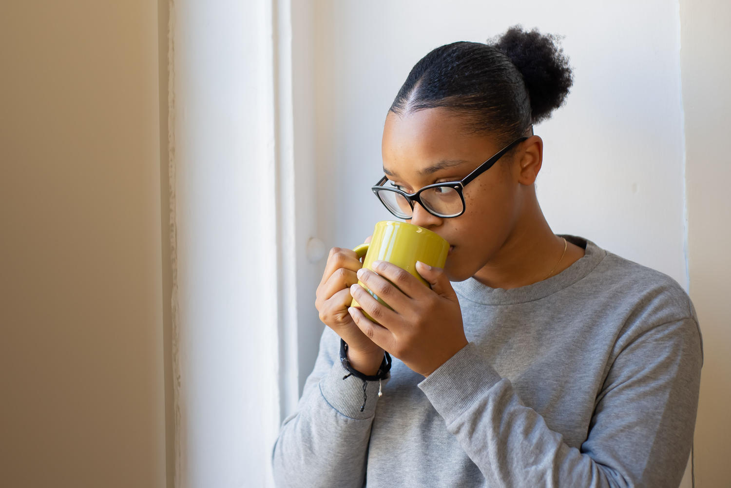 A woman pausing for a quiet moment with a cup of coffee by a window