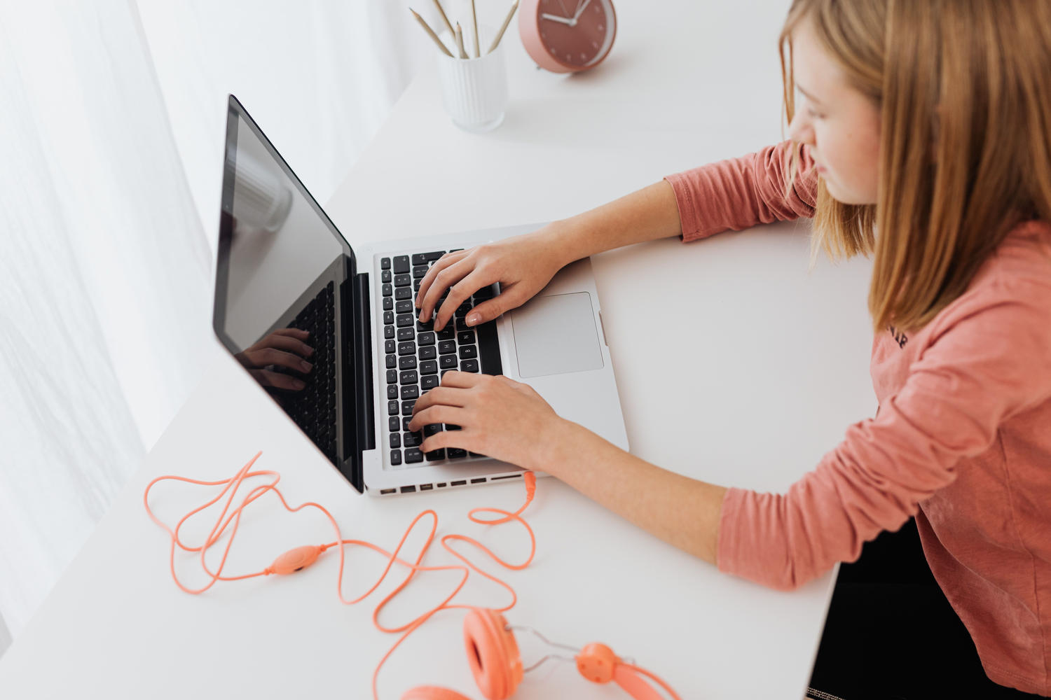 A teen typing on a laptop at a desk, seen from overhead