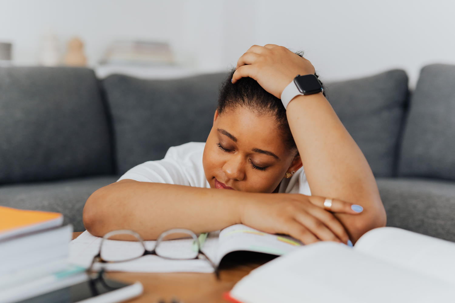 A student resting her head on her arm over an open book on the couch