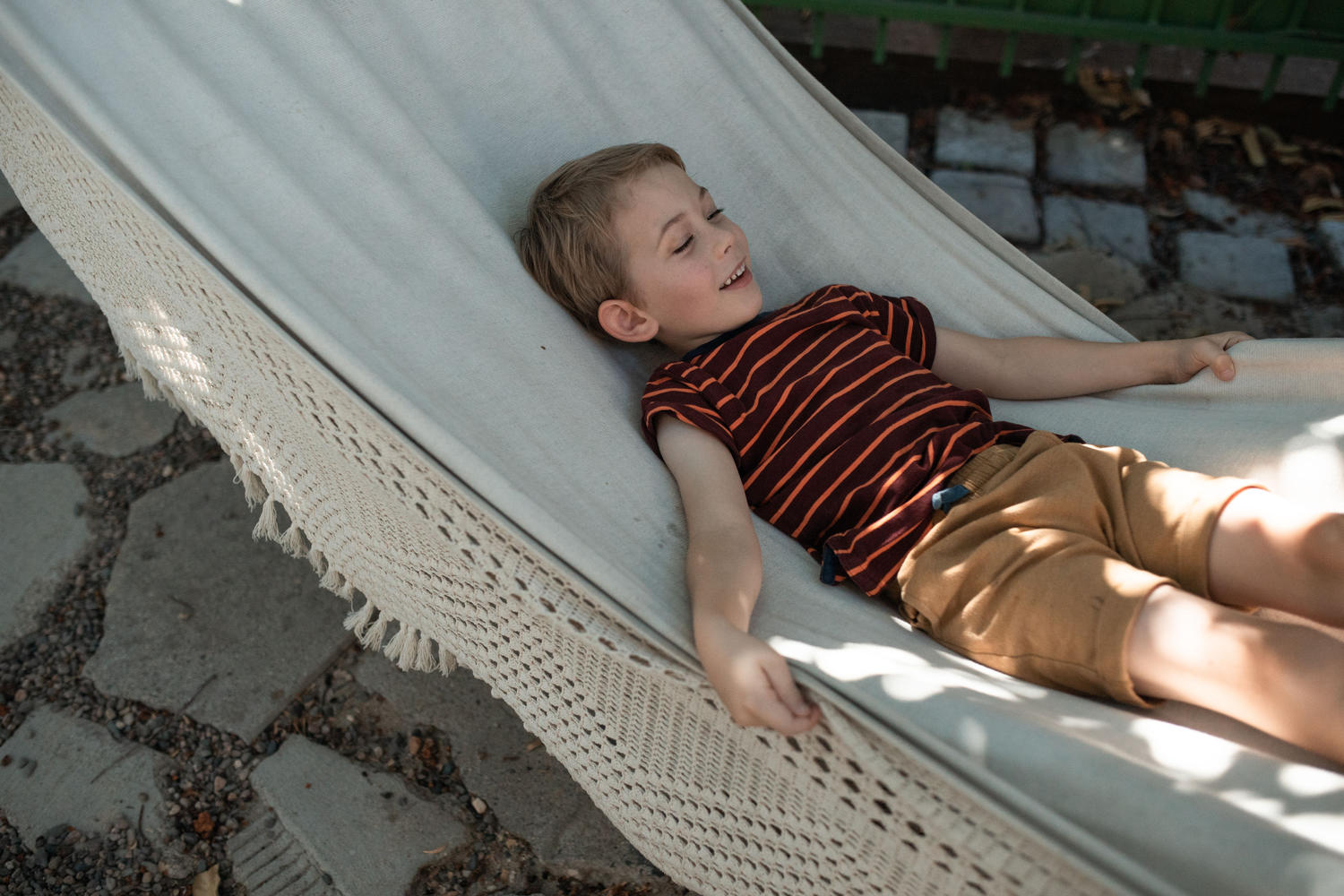 A boy laughing and stretched out in a hammock on a sunny patio